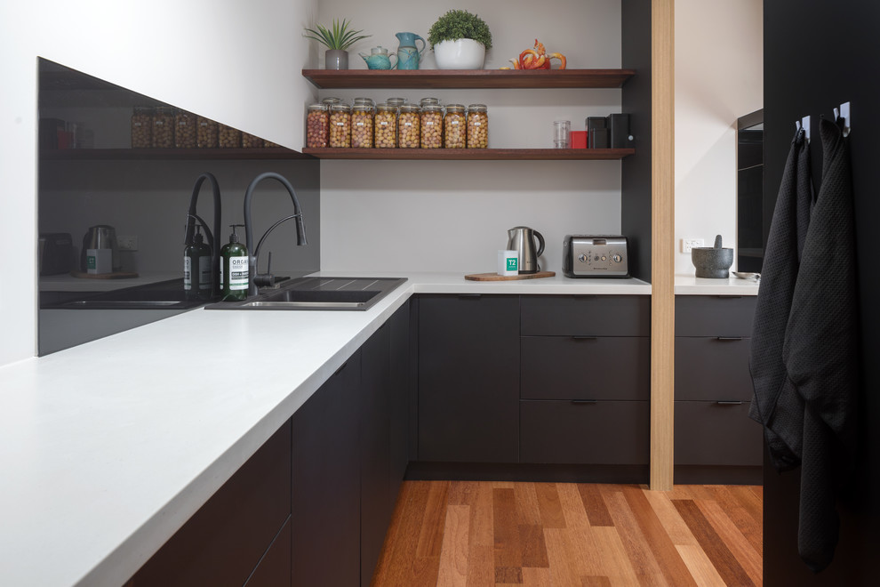 Cette image montre une cuisine minimaliste avec un évier 2 bacs, un placard à porte plane, des portes de placard noires, un plan de travail en quartz modifié, une crédence noire, une crédence en feuille de verre et un plan de travail gris.