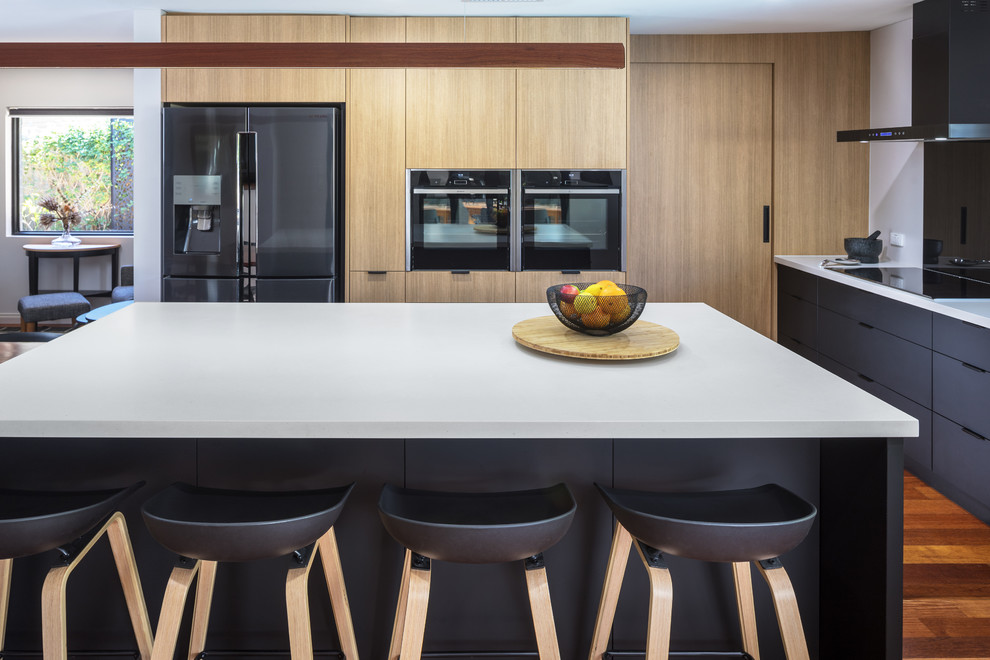 Immagine di un cucina con isola centrale moderno con ante lisce, ante nere, top in quarzo composito, paraspruzzi nero, paraspruzzi con lastra di vetro, elettrodomestici neri e top grigio