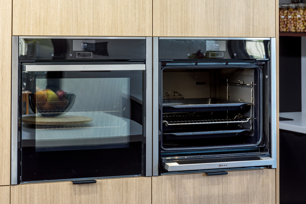 Moderne Küche mit flächenbündigen Schrankfronten, hellen Holzschränken und schwarzen Elektrogeräten in Perth
