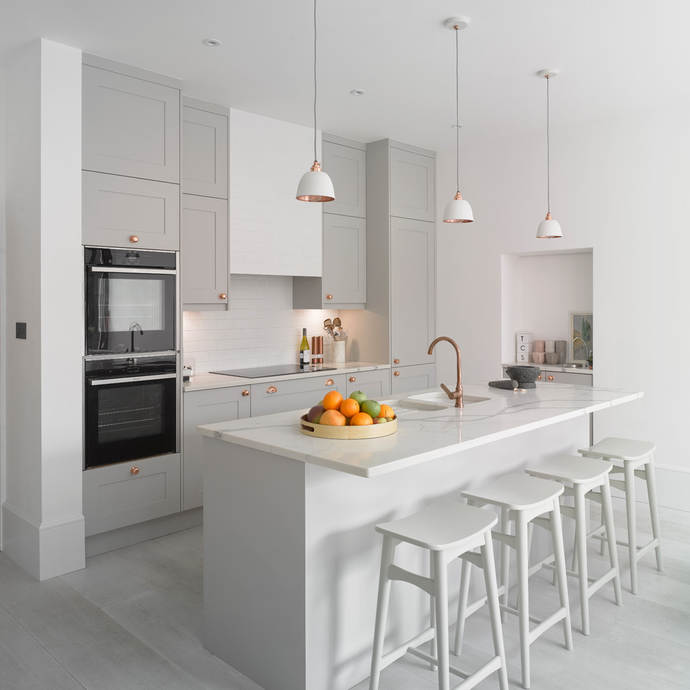 Foto på ett minimalistiskt vit kök, med en dubbel diskho, skåp i shakerstil, grå skåp, vitt stänkskydd, svarta vitvaror, en köksö och grått golv