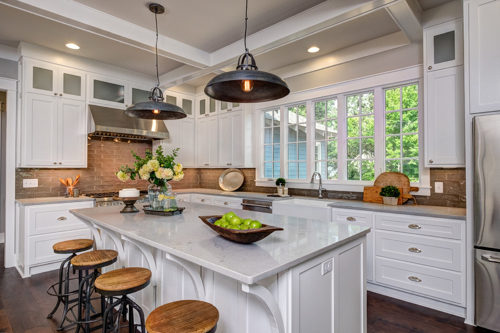 Inspiration for a large timeless l-shaped medium tone wood floor and brown floor eat-in kitchen remodel in Little Rock with a farmhouse sink, shaker cabinets, white cabinets, marble countertops, brown backsplash, subway tile backsplash, stainless steel appliances and an island