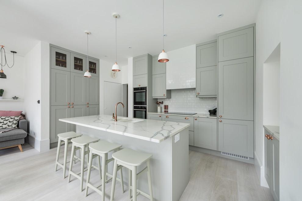 Design ideas for a medium sized traditional l-shaped open plan kitchen in London with shaker cabinets, grey cabinets, quartz worktops, white splashback, metro tiled splashback, stainless steel appliances, light hardwood flooring, an island, grey floors and a submerged sink.