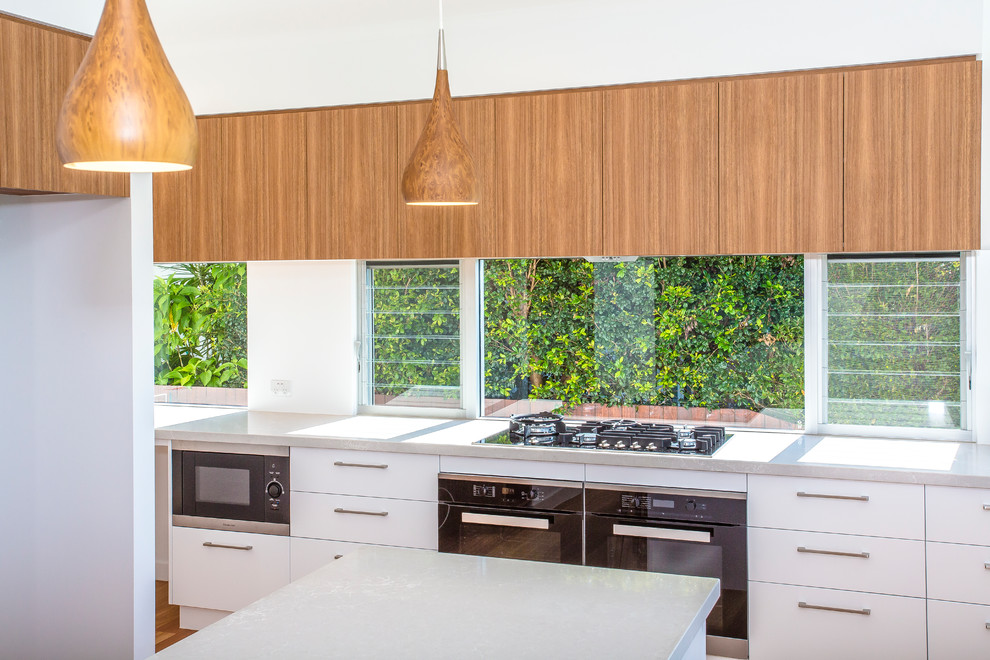 Idéer för ett avskilt, stort modernt l-kök, med en dubbel diskho, släta luckor, vita skåp, bänkskiva i kvarts, fönster som stänkskydd, rostfria vitvaror, ljust trägolv, en köksö och brunt golv
