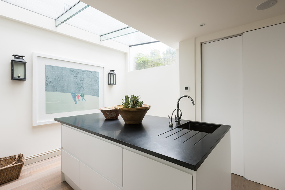This is an example of a small romantic open plan kitchen in London with a built-in sink, flat-panel cabinets, white cabinets, granite worktops, stainless steel appliances, light hardwood flooring and an island.