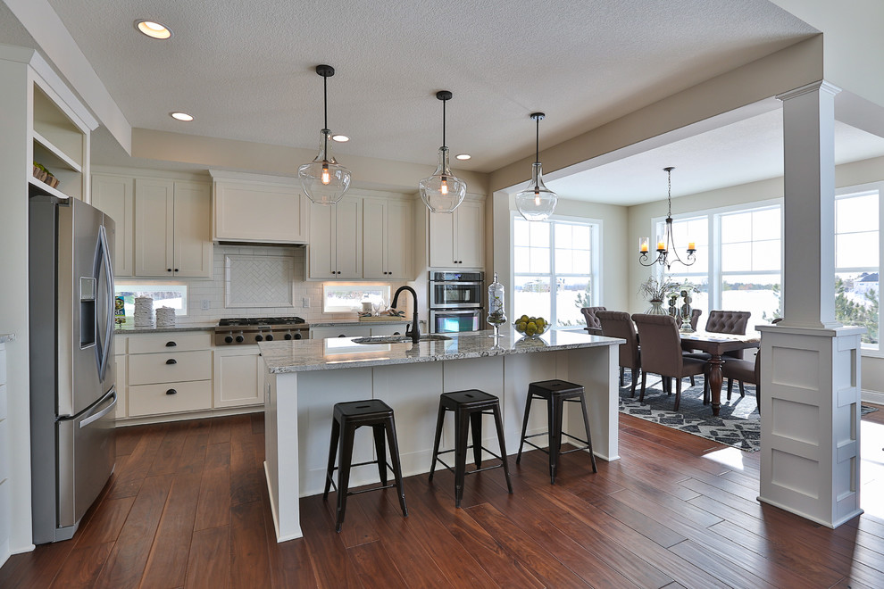 Inspiration for a mid-sized timeless l-shaped medium tone wood floor eat-in kitchen remodel in Minneapolis with a double-bowl sink, recessed-panel cabinets, white cabinets, granite countertops, white backsplash, glass tile backsplash, stainless steel appliances and an island