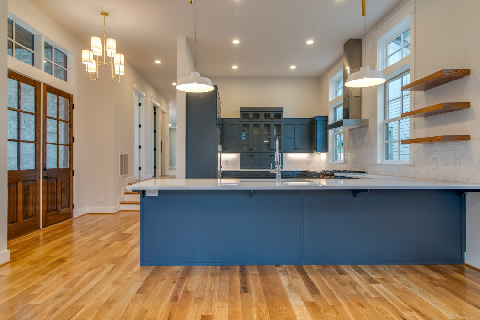 Large transitional u-shaped light wood floor open concept kitchen photo in Nashville with an undermount sink, recessed-panel cabinets, blue cabinets, quartz countertops, white backsplash, marble backsplash, stainless steel appliances, a peninsula and white countertops