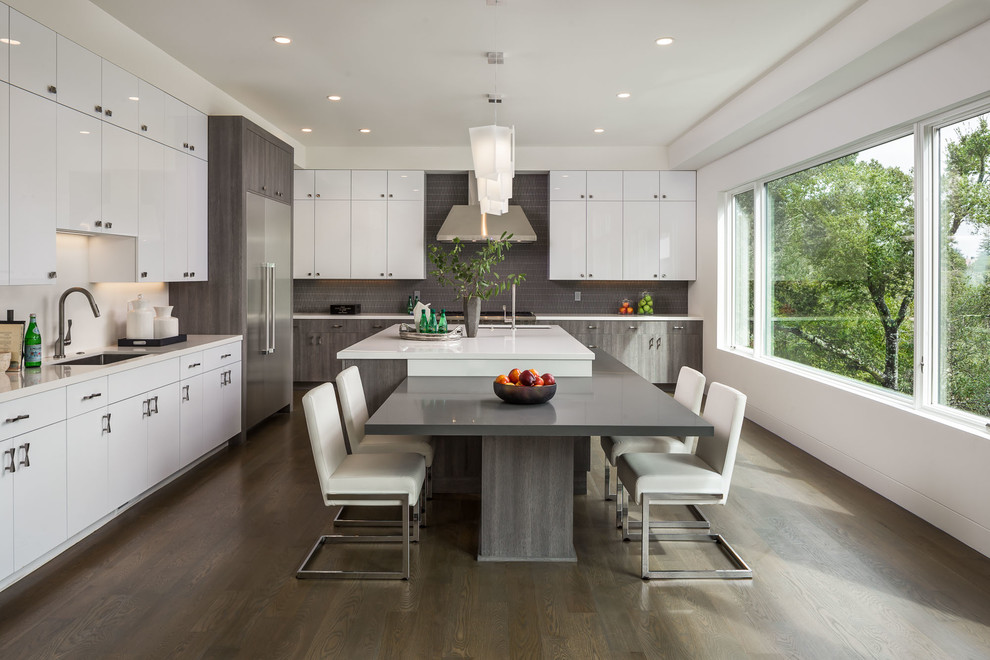 Immagine di una cucina design con lavello sottopiano, ante lisce, ante bianche, paraspruzzi grigio, elettrodomestici in acciaio inossidabile, parquet scuro, pavimento marrone e top bianco