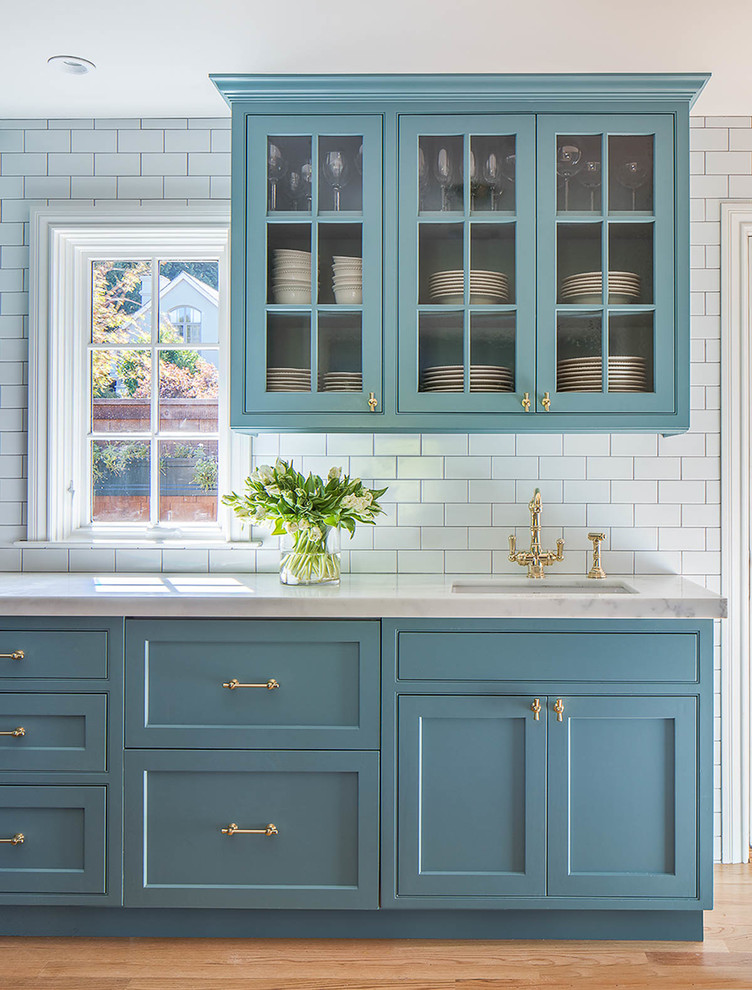 Bild på ett stort funkis l-kök, med luckor med infälld panel, blå skåp, marmorbänkskiva, vitt stänkskydd, stänkskydd i stenkakel, mellanmörkt trägolv, en köksö och en undermonterad diskho