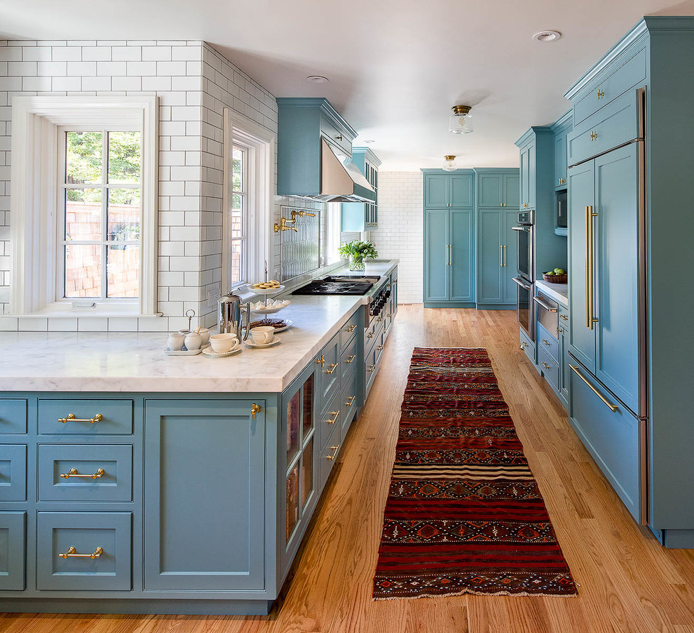 Foto på ett stort funkis l-kök, med luckor med infälld panel, blå skåp, marmorbänkskiva, vitt stänkskydd, stänkskydd i stenkakel, mellanmörkt trägolv och en köksö