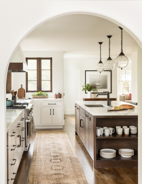 All white kitchen with an arched entryway; vintage rug and stained and white cabinets.