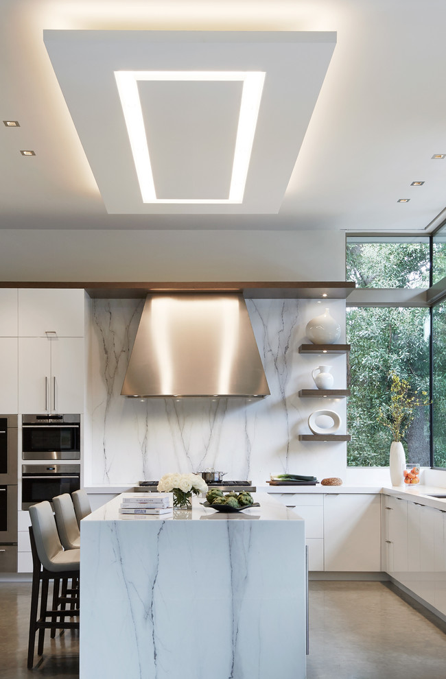 Foto på ett stort funkis vit l-kök, med en enkel diskho, släta luckor, marmorbänkskiva, vitt stänkskydd, stänkskydd i marmor, rostfria vitvaror, betonggolv, en köksö och grått golv