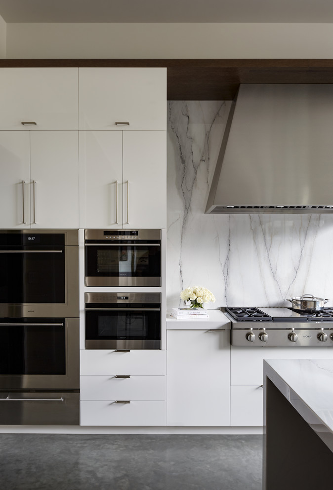 Photo of a large modern u-shaped open plan kitchen in San Francisco with a single-bowl sink, flat-panel cabinets, marble worktops, white splashback, marble splashback, stainless steel appliances, concrete flooring, an island, grey floors and white worktops.