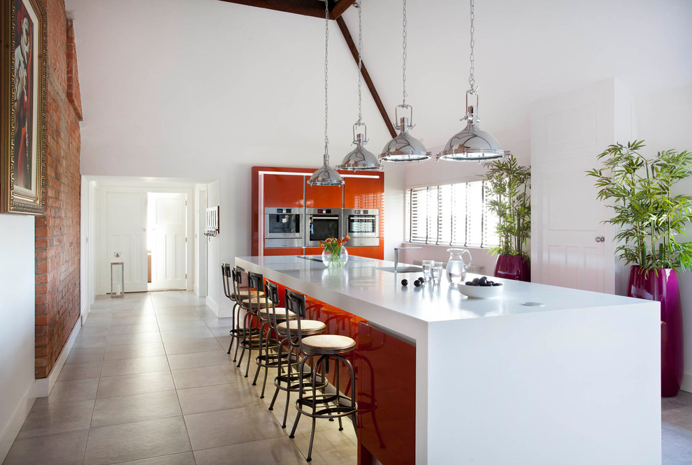 Modern inredning av ett avskilt, stort l-kök, med en undermonterad diskho, släta luckor, orange skåp, bänkskiva i koppar, vitt stänkskydd, stänkskydd i sten, rostfria vitvaror, klinkergolv i keramik, en köksö och grått golv