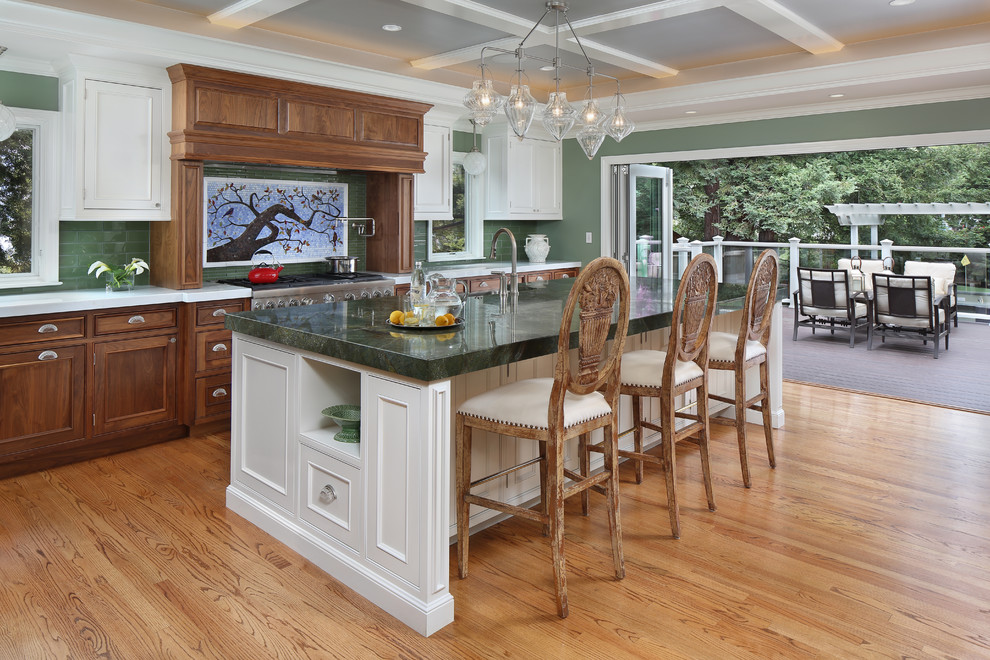 Inredning av ett klassiskt stort grön linjärt grönt kök och matrum, med luckor med profilerade fronter, grönt stänkskydd, stänkskydd i tunnelbanekakel, rostfria vitvaror, en köksö, ljust trägolv och skåp i mellenmörkt trä