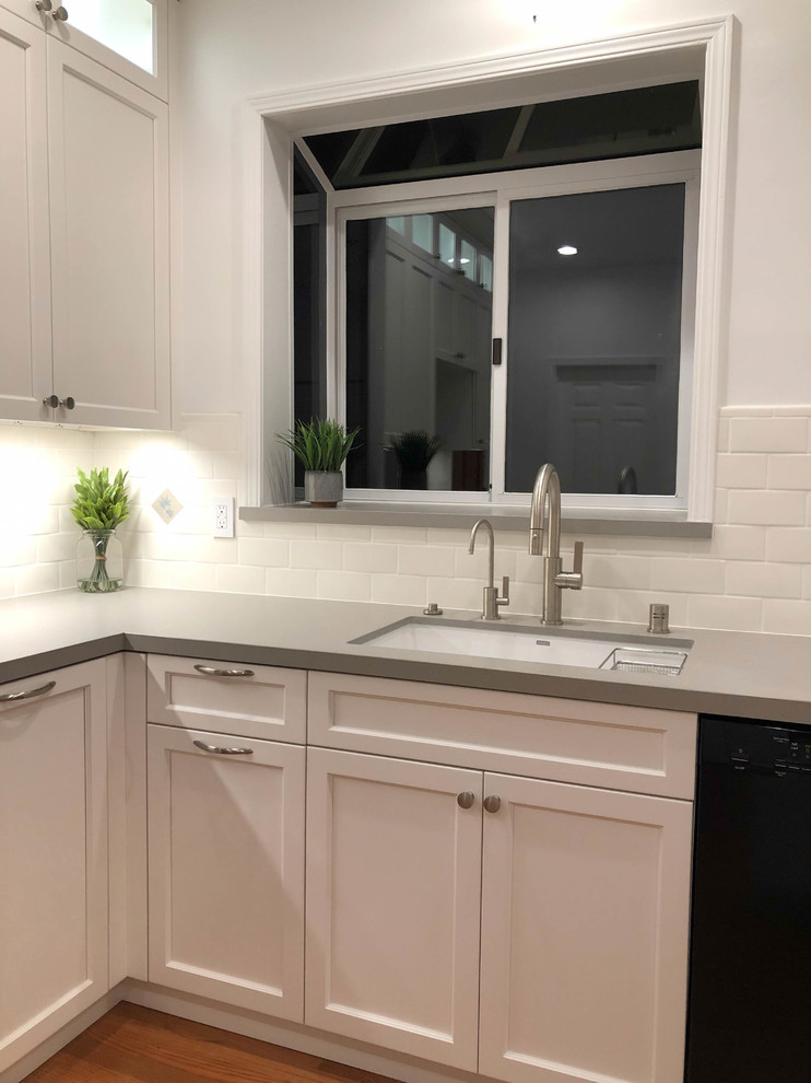Medium sized classic u-shaped kitchen/diner in San Francisco with a submerged sink, recessed-panel cabinets, white cabinets, engineered stone countertops, white splashback, ceramic splashback, stainless steel appliances, medium hardwood flooring, an island, brown floors and grey worktops.