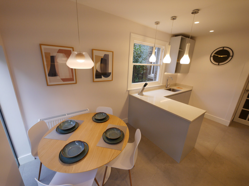 This is an example of a medium sized contemporary galley enclosed kitchen in London with a submerged sink, flat-panel cabinets, blue cabinets, quartz worktops, white splashback, ceramic splashback, black appliances, ceramic flooring, a breakfast bar, grey floors and white worktops.