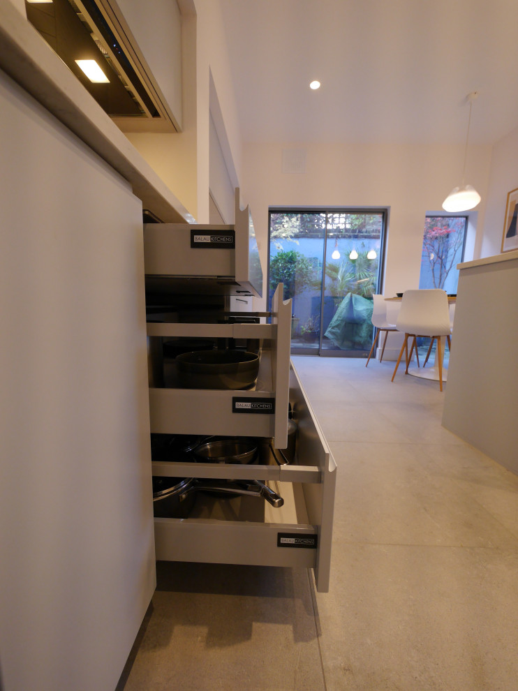 Photo of a medium sized contemporary galley enclosed kitchen in London with a submerged sink, flat-panel cabinets, blue cabinets, quartz worktops, white splashback, ceramic splashback, black appliances, ceramic flooring, a breakfast bar, grey floors and white worktops.