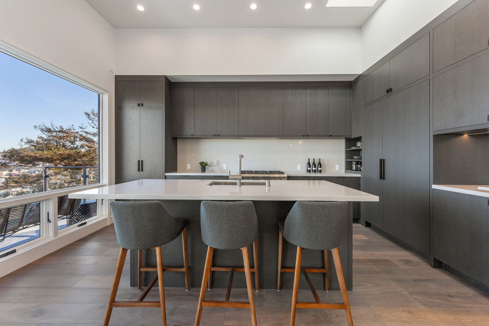Inspiration for a contemporary l-shaped kitchen in San Francisco with a submerged sink, flat-panel cabinets, grey cabinets, integrated appliances, dark hardwood flooring, an island, brown floors and white worktops.