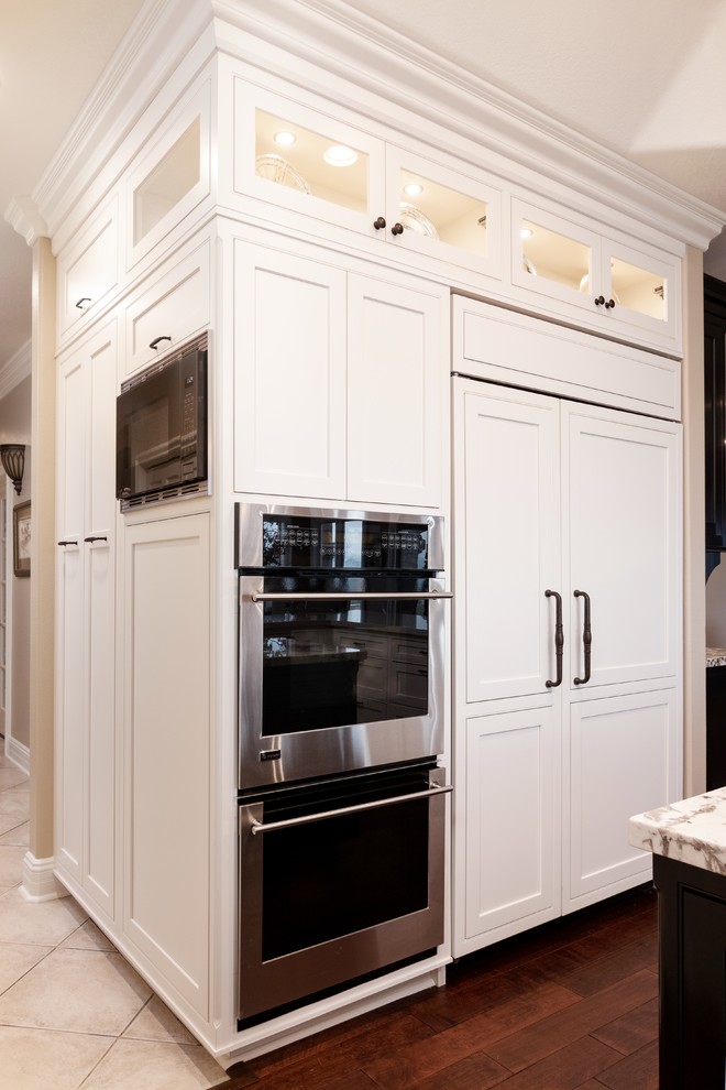 This is an example of a large traditional open plan kitchen in Los Angeles with a single-bowl sink, beaded cabinets, white cabinets, engineered stone countertops, beige splashback, stone tiled splashback, integrated appliances, medium hardwood flooring, an island, brown floors and white worktops.