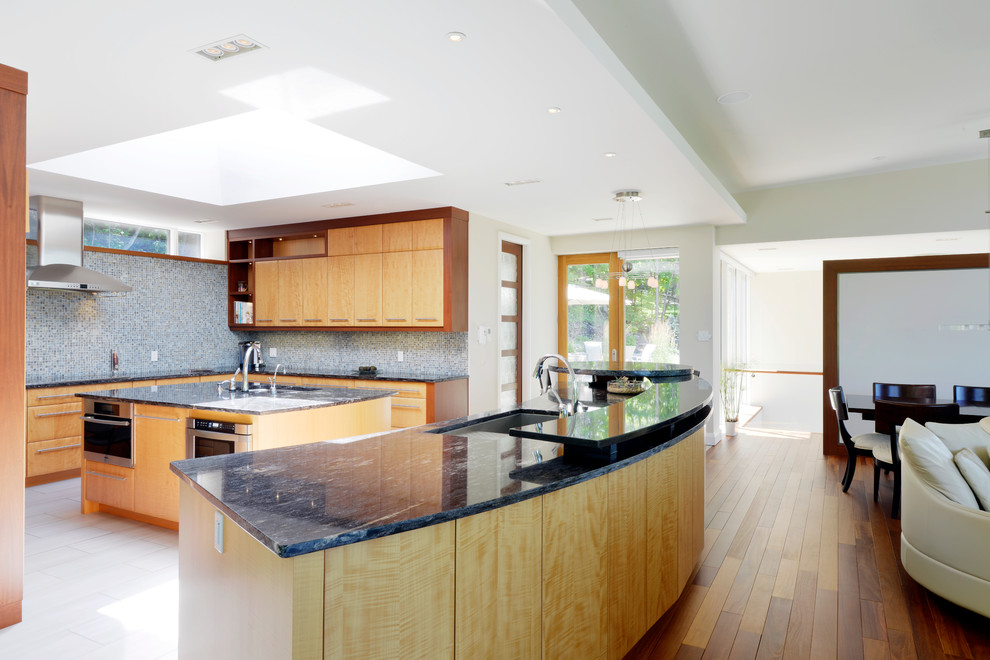 Cette image montre une cuisine design en bois clair avec un évier encastré, un placard à porte plane, une crédence bleue, un électroménager en acier inoxydable et une crédence en mosaïque.