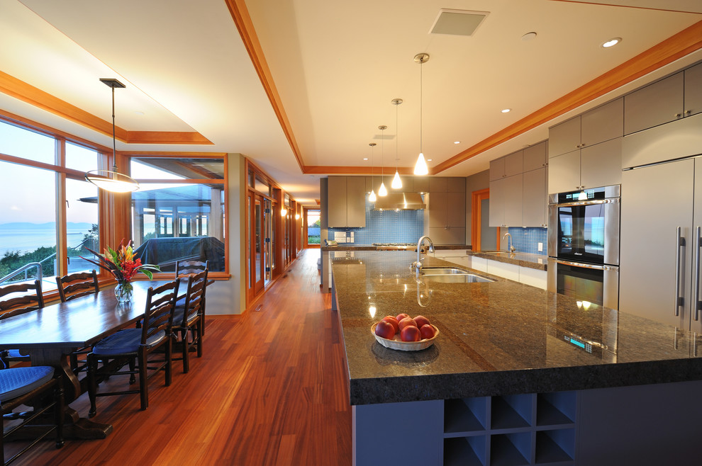 Example of a large trendy l-shaped medium tone wood floor and brown floor eat-in kitchen design in Vancouver with an undermount sink, granite countertops, blue backsplash, ceramic backsplash, stainless steel appliances, an island, flat-panel cabinets and gray cabinets