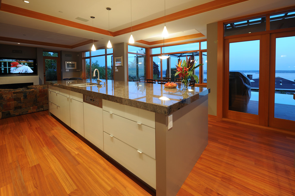 Große Moderne Wohnküche in L-Form mit Unterbauwaschbecken, Glasfronten, Granit-Arbeitsplatte, braunem Holzboden, Kücheninsel, grauen Schränken, Küchenrückwand in Blau, Rückwand aus Keramikfliesen, Küchengeräten aus Edelstahl und braunem Boden in Vancouver