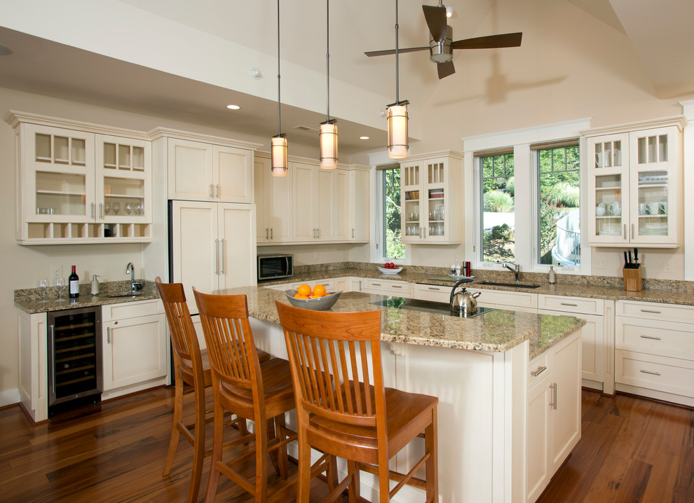 Modern inredning av ett kök, med en undermonterad diskho, luckor med infälld panel, vita skåp, granitbänkskiva, beige stänkskydd, rostfria vitvaror, mörkt trägolv och en köksö