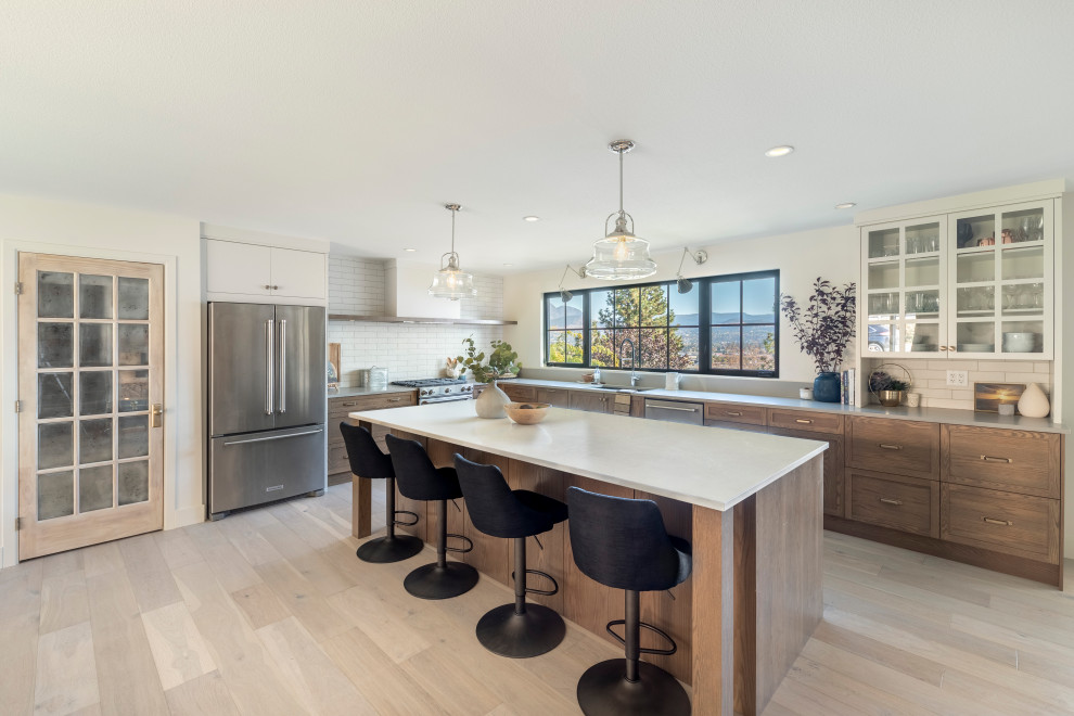 Photo of a large farmhouse l-shaped kitchen/diner in Vancouver with medium wood cabinets, engineered stone countertops, white splashback, metro tiled splashback, stainless steel appliances, light hardwood flooring, an island, a submerged sink, shaker cabinets, beige floors and grey worktops.