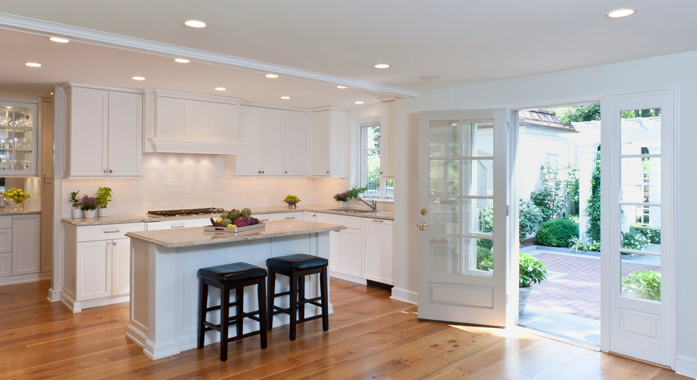 Example of a mid-sized classic l-shaped light wood floor and brown floor open concept kitchen design in Philadelphia with shaker cabinets, white cabinets, white backsplash, an undermount sink, granite countertops, subway tile backsplash, stainless steel appliances and an island