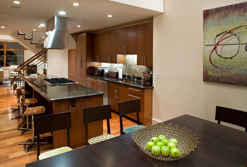 Bild på ett funkis kök, med integrerade vitvaror, släta luckor, skåp i mellenmörkt trä, stänkskydd i mosaik, flerfärgad stänkskydd, en undermonterad diskho, granitbänkskiva och ljust trägolv