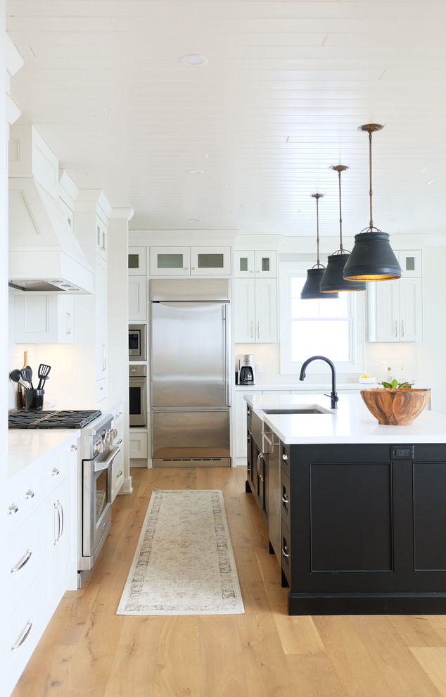 Inspiration for a farmhouse light wood floor kitchen remodel in Toronto with a farmhouse sink, shaker cabinets, white cabinets, quartzite countertops, white backsplash, subway tile backsplash, stainless steel appliances, an island and white countertops