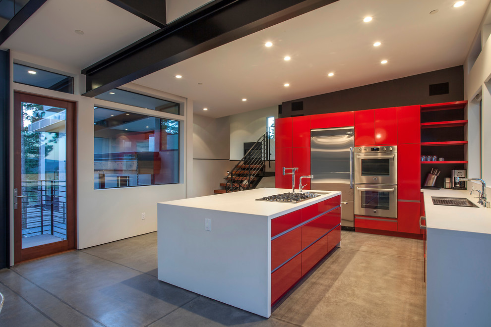 Diseño de cocinas en L contemporánea con armarios con paneles lisos, puertas de armario rojas, electrodomésticos de acero inoxidable, suelo de cemento y una isla