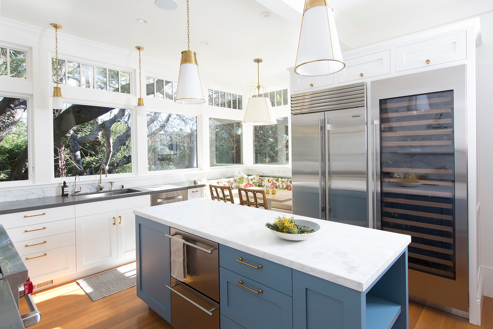 Inspiration for a medium sized traditional u-shaped kitchen/diner in San Francisco with a built-in sink, shaker cabinets, white cabinets, marble worktops, white splashback, marble splashback, light hardwood flooring, an island, grey worktops, stainless steel appliances and brown floors.