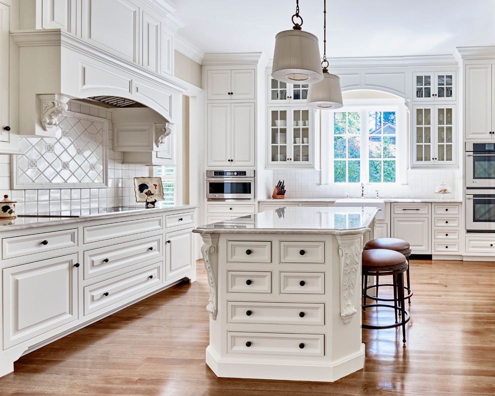 Inspiration for a traditional l-shaped kitchen in Raleigh with a belfast sink, raised-panel cabinets, white cabinets, white splashback, light hardwood flooring and an island.