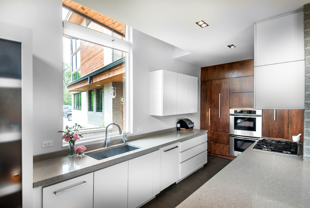 Exempel på ett mellanstort modernt kök, med en undermonterad diskho, släta luckor, vita skåp, rostfria vitvaror, en köksö, granitbänkskiva, kalkstensgolv och beiget golv