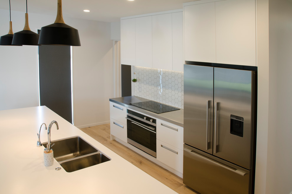 Modern inredning av ett stort vit vitt kök, med en nedsänkt diskho, öppna hyllor, vita skåp, laminatbänkskiva, vitt stänkskydd, stänkskydd i tunnelbanekakel, rostfria vitvaror, ljust trägolv och brunt golv