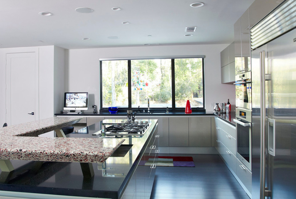 Bild på ett stort funkis kök, med en undermonterad diskho, släta luckor, bänkskiva i återvunnet glas, rött stänkskydd, stänkskydd i metallkakel, vita vitvaror, mörkt trägolv och en köksö