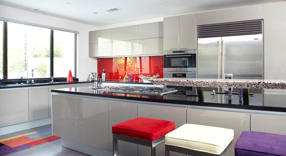 Modern inredning av ett stort kök, med en undermonterad diskho, släta luckor, rött stänkskydd, stänkskydd i metallkakel, vita vitvaror, mörkt trägolv och en köksö