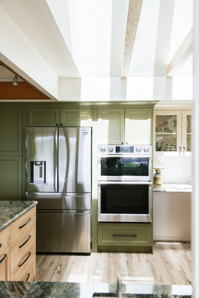 Bild på ett mellanstort vintage blå blått kök, med en dubbel diskho, luckor med infälld panel, skåp i ljust trä, granitbänkskiva, vitt stänkskydd, stänkskydd i tunnelbanekakel, rostfria vitvaror, vinylgolv, en halv köksö och flerfärgat golv