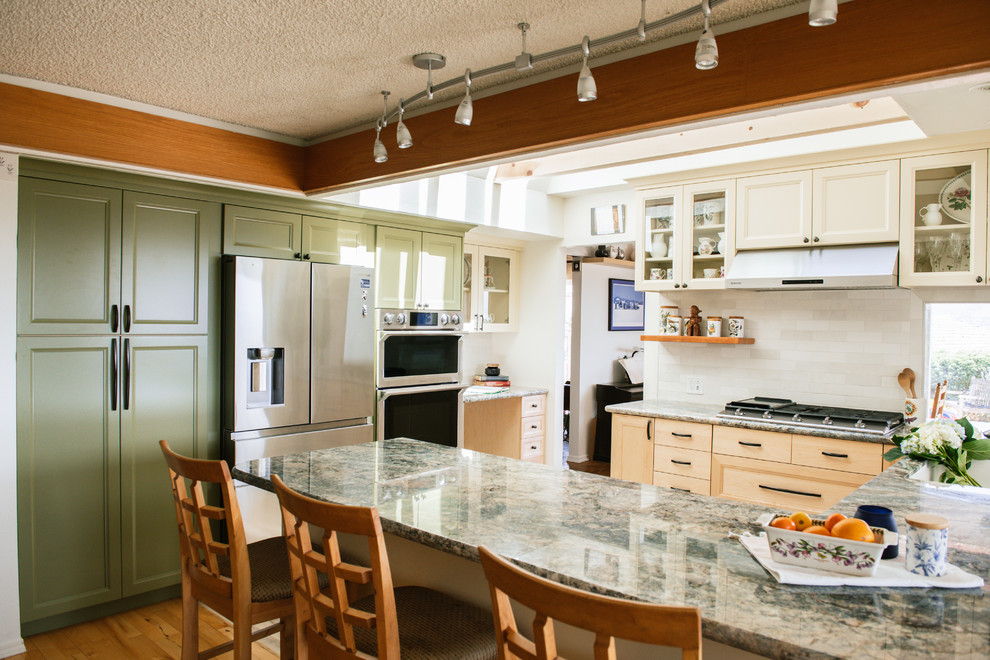 Inredning av ett klassiskt mellanstort blå blått kök, med en dubbel diskho, luckor med infälld panel, skåp i ljust trä, granitbänkskiva, vitt stänkskydd, stänkskydd i tunnelbanekakel, rostfria vitvaror, vinylgolv, en halv köksö och flerfärgat golv