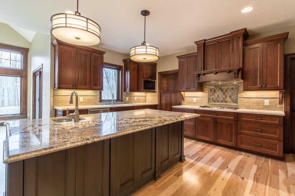 Example of a large arts and crafts u-shaped medium tone wood floor eat-in kitchen design in Cleveland with an undermount sink, recessed-panel cabinets, medium tone wood cabinets, quartzite countertops, beige backsplash, stone tile backsplash, stainless steel appliances and an island