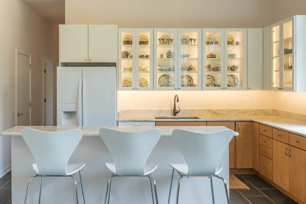 Свежая идея для дизайна: угловая кухня-гостиная в стиле модернизм с врезной мойкой, стеклянными фасадами, белыми фасадами, гранитной столешницей, бежевым фартуком, белой техникой и островом - отличное фото интерьера