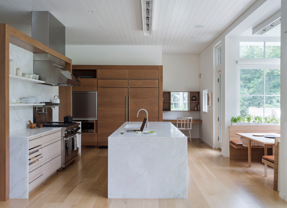 Photo of a contemporary l-shaped open plan kitchen in Boston with a submerged sink, flat-panel cabinets, medium wood cabinets, white splashback, stone slab splashback, stainless steel appliances, light hardwood flooring, an island and beige floors.