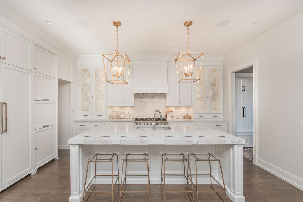 This is an example of a traditional l-shaped kitchen in Chicago with shaker cabinets, white cabinets, white splashback, integrated appliances, medium hardwood flooring, an island, brown floors and white worktops.