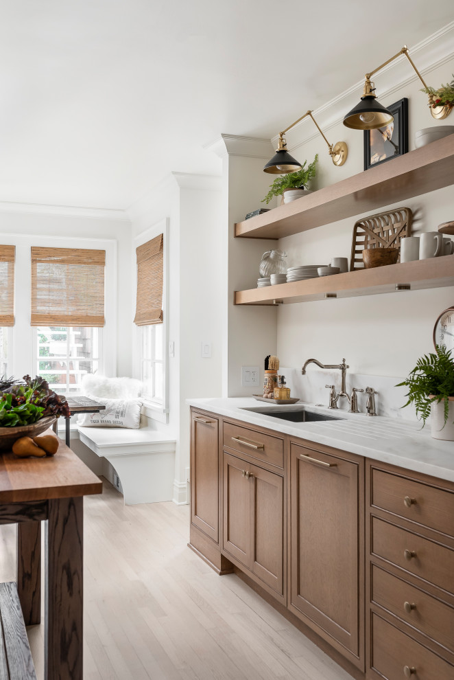 Foto de cocina clásica de tamaño medio cerrada con fregadero encastrado, armarios con rebordes decorativos, puertas de armario de madera oscura, encimera de mármol, salpicadero metalizado, salpicadero con efecto espejo, electrodomésticos de acero inoxidable, suelo de madera clara, una isla, suelo marrón y encimeras blancas