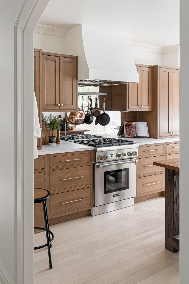 Medium sized classic galley enclosed kitchen in Chicago with a built-in sink, beaded cabinets, medium wood cabinets, marble worktops, metallic splashback, mirror splashback, stainless steel appliances, light hardwood flooring, an island, brown floors and white worktops.