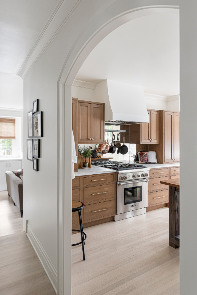 Inspiration for a mid-sized timeless galley light wood floor and brown floor enclosed kitchen remodel in Chicago with a drop-in sink, beaded inset cabinets, medium tone wood cabinets, marble countertops, metallic backsplash, mirror backsplash, stainless steel appliances, an island and white countertops