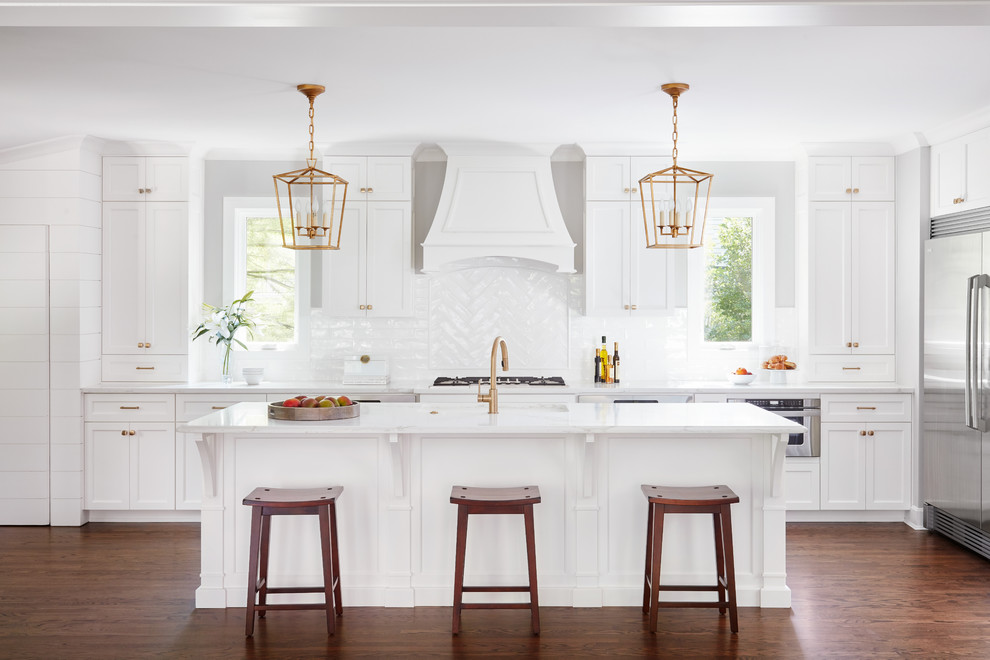 Exempel på ett stort klassiskt kök, med skåp i shakerstil, vita skåp, vitt stänkskydd, rostfria vitvaror, en köksö, en undermonterad diskho, marmorbänkskiva, stänkskydd i porslinskakel, mörkt trägolv och brunt golv