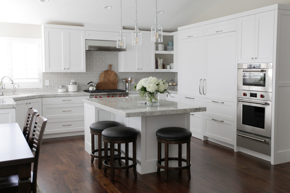 Exempel på ett klassiskt grå grått l-kök, med luckor med infälld panel, vita skåp, grått stänkskydd, stänkskydd i tunnelbanekakel, rostfria vitvaror, mörkt trägolv, en köksö och brunt golv