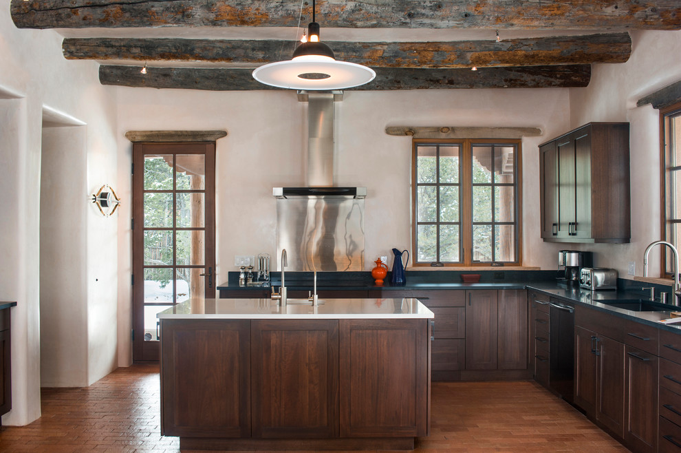 Aménagement d'une grande cuisine américaine sud-ouest américain en L et bois foncé avec un évier 1 bac, un placard à porte shaker, une crédence métallisée, un sol en bois brun et îlot.
